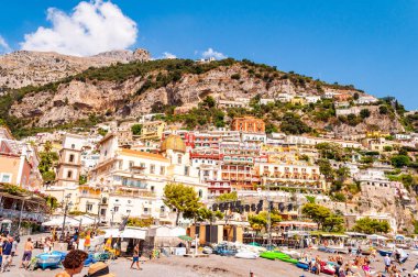 Ortaçağ Positano 'sunun kayalık manzarası, plajdaki insanlar, rahat caddelerde yürüyen turistler ve apartman ve iş yerleriyle dolu gezinti yerleri.