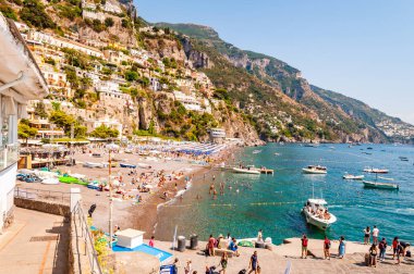 İnanılmaz Positano şehri kayalık arazide, plajdaki insanlar, tekneler deniz turlarına gelip gidiyor, apartmanlar ve iş yerleriyle dolu gezinti alanları.