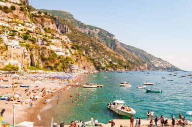 İnanılmaz Positano şehri kayalık arazide, plajdaki insanlar, tekneler deniz turlarına gelip gidiyor, apartmanlar ve iş yerleriyle dolu gezinti alanları.