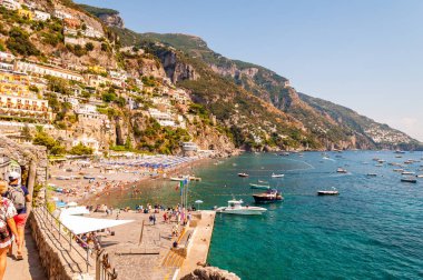 İnanılmaz Positano şehri kayalık arazide, plajdaki insanlar, tekneler deniz turlarına gelip gidiyor, apartmanlar ve iş yerleriyle dolu gezinti alanları.