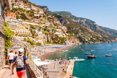 İnanılmaz Positano şehri kayalık arazide, plajdaki insanlar, tekneler deniz turlarına gelip gidiyor, apartmanlar ve iş yerleriyle dolu gezinti alanları.