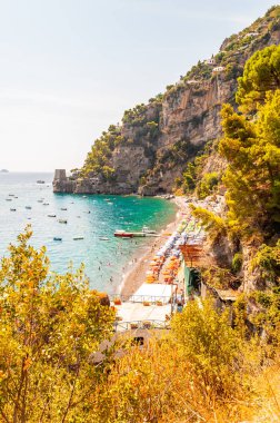 Positano şehri kayalık arazide, plajdaki insanlar, tekneler deniz turlarına gelip gidiyor, kayalık dağın kenarındaki manzaralı gezinti alanı her yer yeşil ağaç ve bitkilerle çevrili.