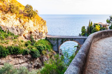 Campania bölgesindeki Tyrhenian körfezi üzerindeki yüksek kayalık uçurumlar arasında inşa edilen Fiordo di Furore ark köprüsünün görüntüsü. Dağda, eşsiz doğa geçidinin etrafındaki kıvrımlı yürüyüş yolu.