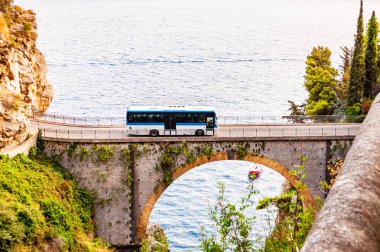 Campania bölgesindeki Tyrhenian körfezi üzerindeki yüksek kayalık uçurumlar arasında inşa edilen Fiordo di Furore ark köprüsünün görüntüsü. Köprüde otobüs sürüyor, teknesi eşsiz bir koyda yüzüyor.