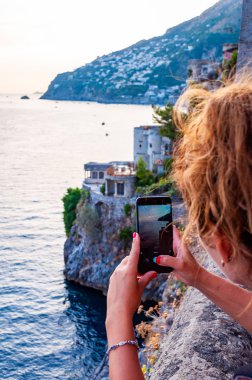 Positano, İtalya - 05 Eylül 2019: Campania 'nın Fiordo di Furore ve Positano bölgesinde akıllı telefonuyla deniz manzarası çeken kadın turist