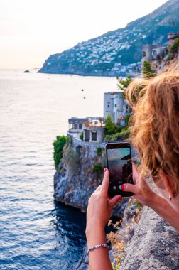 Positano, İtalya - 05 Eylül 2019: Campania 'nın Fiordo di Furore ve Positano bölgesinde akıllı telefonuyla deniz manzarası çeken kadın turist