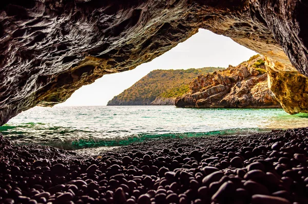 Increíble vista del paisaje marino desde una cueva marina única que sobresale sobre el agua en el famoso entorno escénico de la playa de Cala Bianca. Olas cristalinas de agua de mar lavando guijarros dentro de la cueva rocosa masiva — Foto de Stock