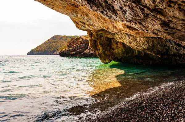 Дивовижний вигляд морського плавця з унікальної морської печери нависає над водою на знаменитому мальовничому краєвиді пляжу Кала Б "янка. Кришталеві чисті морські хвилі промивають камінці в масивній кам "янистій печері — стокове фото
