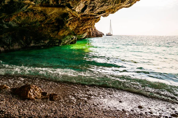 Дивовижний вигляд морського плавця з унікальної морської печери нависає над водою на знаменитому пляжному мальовничому оточенні Кала Б'янка з плаваючою морською яхтою, що плаває на фоні. Італійські моря. — стокове фото
