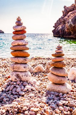 Sahilde iki tane düz taş kule. Taş dengeleme, taşların doğal olarak farklı pozisyonlarda üst üste dengelendiği sanat disiplini veya hobisidir. Cala Bianca İtalya