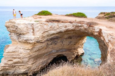 Kayanın kenarındaki turistler. Torre Sant Andrea plajı yumuşak nasırlı kayaları ve uçurumları, deniz yığınları, küçük koyları ve pürüzlü kıyı manzarasıyla