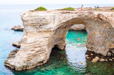 Kayanın kenarındaki turistler. Torre Sant Andrea plajı yumuşak nasırlı kayaları ve uçurumları, deniz yığınları, küçük koyları ve pürüzlü kıyı manzarasıyla
