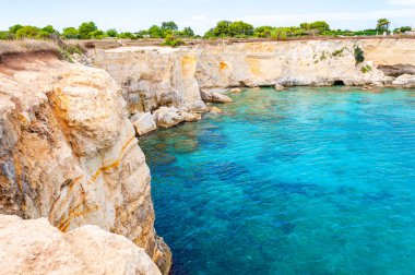 Torre Sant Andrea sahilinde kristal berrak su ve pürüzlü kıyı manzarası. İtalya, Melendugno 'daki İyon Denizi Koyu