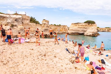 İnsanlar uçurumdan atlıyor, güneşleniyor, kristal berrak deniz suyunda yüzüyor kayalık sahilde Torre Sant Andrea 'da kayalar, kayalıklar ve deniz yığınları var.