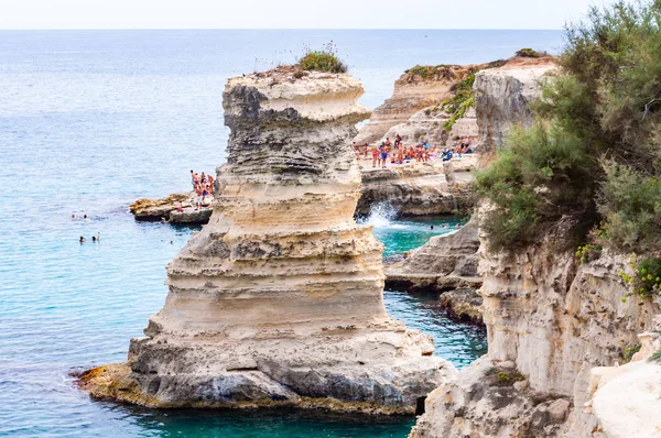Люди ныряют с плоской скалы, загорают, купаются в кристально чистой морской воде на скалистом пляже Torre Sant Andrea со скалами, скалами и морскими стеками — стоковое фото