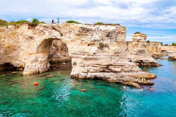 Gente buceando desde el acantilado, tomando el sol, nadando en aguas cristalinas en la playa rocosa Torre Sant Andrea con rocas, acantilados y pilas de mar — Foto de Stock