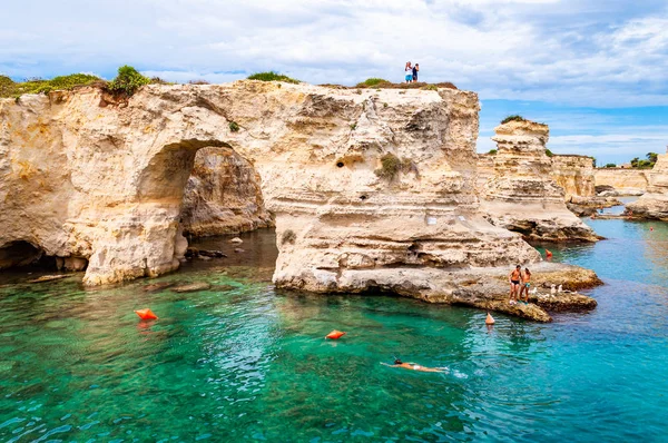 Άνθρωποι που καταδύονται από τον γκρεμό, κάνουν ηλιοθεραπεία, κολυμπούν σε κρυστάλλινα νερά στη βραχώδη παραλία Torre Sant Andrea με βράχια, γκρεμούς και θαλάσσιες στοίβες — Φωτογραφία Αρχείου