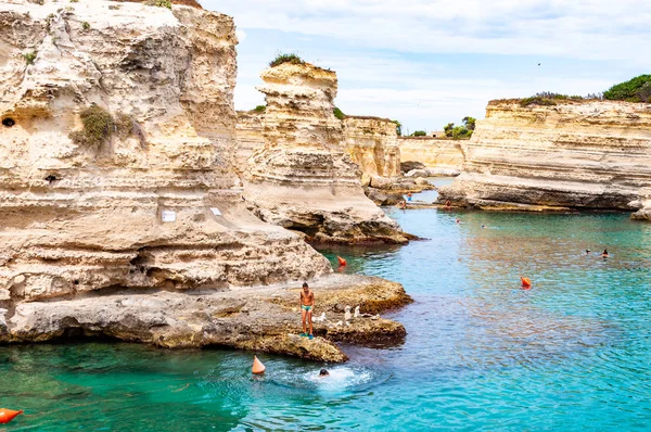 Люди ныряют со скалы, загорают, купаются в кристально чистой морской воде на скалистом пляже Torre Sant Andrea со скалами, скалами и морскими стеками — стоковое фото
