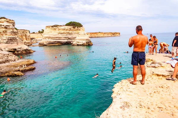 Люди ныряют со скалы, загорают, купаются в кристально чистой морской воде на скалистом пляже Torre Sant Andrea со скалами, скалами и морскими стеками — стоковое фото