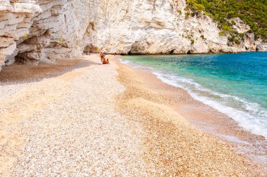 Etrafı yüksek kayalık kayalıklarla çevrili güzel çakıl taşı sahillerindeki insanlar ve Gargano Adriyatik sahil şeridinin ünlü deniz yığınları.