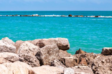 Plajda, Spiaggia del Frate ve Adriyatik deniz dalgaları ve akıntıları arasında bir sınır olarak uzanan devasa kayalar. Arka planda dalgakıran iskelesi olarak Rocky marinası var. İtalya