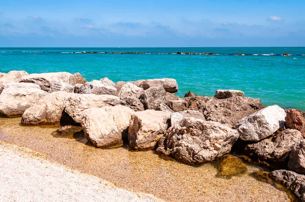 Масивні камені лежать на пляжі як кордон між піщаним пляжем Spiaggia del Frate і Адріатичними морськими хвилями і потоками. Rocky marina як пірс з водою на задньому плані. Італія — стокове фото
