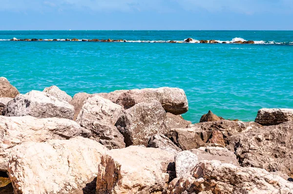 Масивні камені лежать на пляжі як кордон між піщаним пляжем Spiaggia del Frate і Адріатичними морськими хвилями і потоками. Rocky marina як пірс з водою на задньому плані. Італія — стокове фото