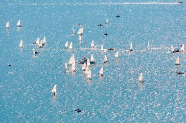 Yelkencilik eğitimine yukarıdan bak. Birçok yelkenli, gölün mavi sularında pratik yapar. Bir grup sporcu, beyaz yelkenliler, güçlü rüzgar, güneşli bir gün..