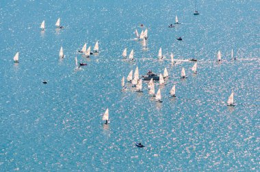 Yelkencilik eğitimine yukarıdan bak. Birçok yelkenli, gölün mavi sularında pratik yapar. Bir grup sporcu, beyaz yelkenliler, güçlü rüzgar, güneşli bir gün..