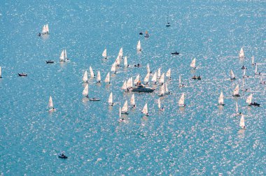Yelkencilik eğitimine yukarıdan bak. Birçok yelkenli, gölün mavi sularında pratik yapar. Bir grup sporcu, beyaz yelkenliler, güçlü rüzgar, güneşli bir gün..