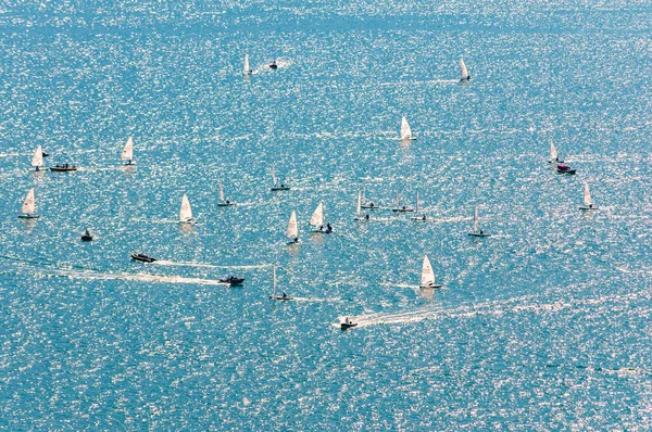 Pohled shora na plachtění školení. Mnoho plachetnic cvičí na modrých vodách jezera. Skupina sportovců, bílé plachty, silný vítr, slunečný den. — Stock fotografie