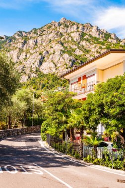 Limone Sul Garda şehrinin sıcacık caddesinde apartmanlar, oteller ve arka planda dolomit dağları olan küçük işletmeler var. Lombardy, İtalya