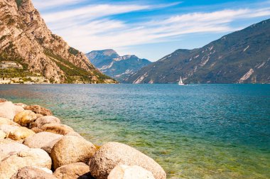 Lombardy, Kuzey İtalya 'daki güzel Garda gölünün kıyısında bulunan yuvarlak kayalar yüksek dolomit dağlarıyla çevrilidir. Gölde yüzen klasik beyaz yelkenli yat.