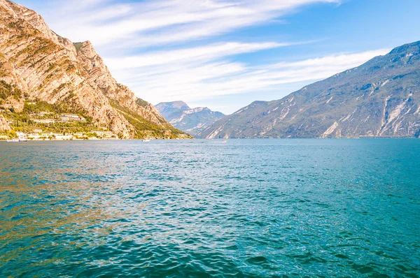 Fantastisk Gardasjö i Lombardiet, Italien omgiven av höga dolomitberg. Båtar och yacht flyter på sjön. Olika hotell och privata hus byggda på den steniga stranden av sjön — Stockfoto