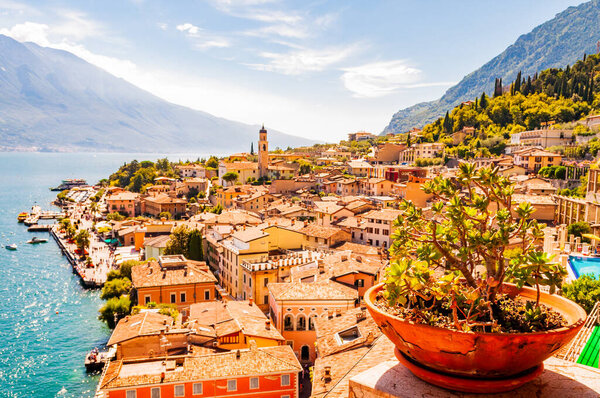 Vibrant succulents growing in a flowerpot on the balcony with Limone Sul Garda cityscape on background. Shore of Garda lake surrounded by scenic Northern Italian nature. Amazing Italian cities