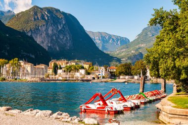 Güzel Riva del Garda şehri. Sahilde ve şehirde arka planda yüksek dolomite dağlarıyla çevrili kırmızı pedallı tekneler var.