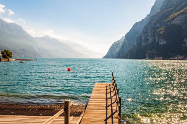 Lombardiya, İtalya 'daki güzel Garda Gölü' nün kuzey kıyısında yüksek dolomit dağları ve gölün kristal berrak mavi suyuyla çevrili ahşap iskele manzarası. Riva