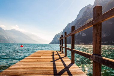 Lombardiya, İtalya 'daki güzel Garda Gölü' nün kuzey kıyısında yüksek dolomit dağları ve gölün kristal berrak mavi suyuyla çevrili ahşap iskele manzarası. Riva
