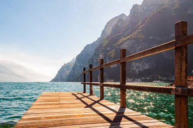 Lombardiya, İtalya 'daki güzel Garda Gölü' nün kuzey kıyısında yüksek dolomit dağları ve gölün kristal berrak mavi suyuyla çevrili ahşap iskele manzarası. Riva