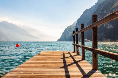Lombardiya, İtalya 'daki güzel Garda Gölü' nün kuzey kıyısında yüksek dolomit dağları ve gölün kristal berrak mavi suyuyla çevrili ahşap iskele manzarası. Riva