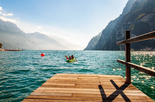 To turister ankommer med kajakk til moloen ved Garda-sjøen i Riva del Garda i Italia, omgitt av høye dolomittfjell – stockfoto