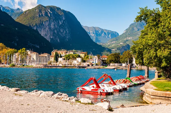 Hermoso paisaje urbano de Riva del Garda con vibrantes botes de pedales rojos estacionados en fila en la playa y la ciudad rodeados de altas montañas de dolomita en el fondo —  Fotos de Stock