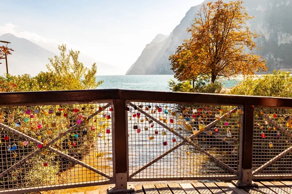 Kärlek och äktenskap lås hängande på metallnät på träräcken i Riva del Garda stad med vacker sjö vattenlandskap på bakgrunden — Stockfoto