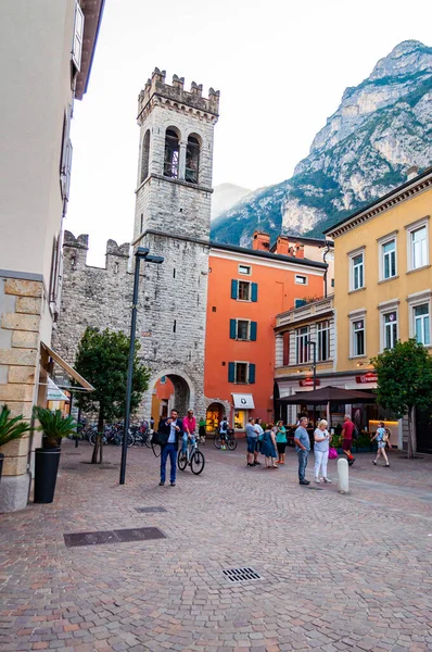 Scénická městská krajina Riva del Garda. Útulná ulice plná turistů, rostlin a italské architektury s vysokými dolomitovými horami na pozadí — Stock fotografie