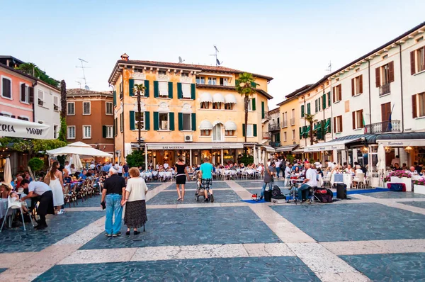 Люди прогуливаются по улицам знаменитого Старого города Сирмионе, расположенного на полуострове озера Гарда в Италии. Площадь с рестораном — стоковое фото