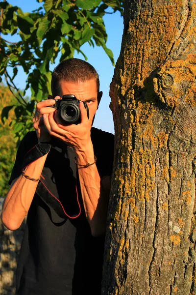 Man Black Shirt Taking Pictures Camera Hidden Tree Trunk Nature — Stock Photo, Image