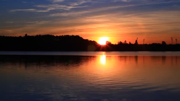 地平線の森のシルエットの後ろに太陽の美しいシーン 日没時に湖の水に反映されている空と非常にカラフルな雲 風景の驚くべき対称性 — ストック動画