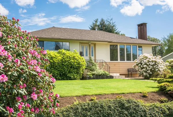Casa familiar media con flores de rododendro delante sobre fondo nublado — Foto de Stock