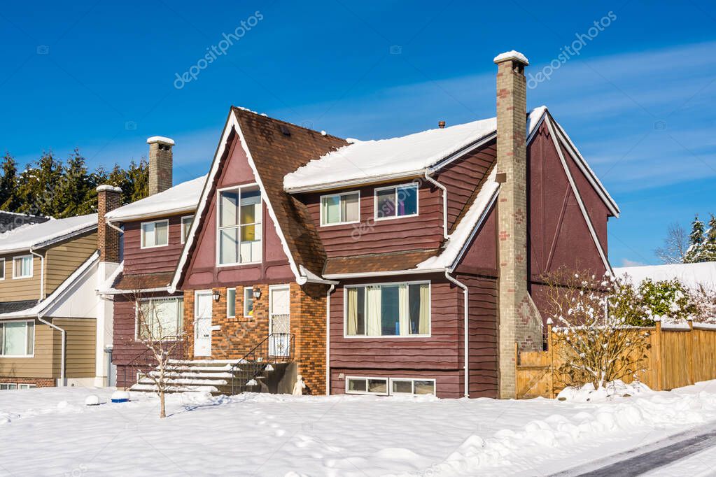 Old modest residential duplex house in snow on sunny winter day