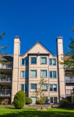 Parlak güneşli bir günde önünde yeşil çimenler olan apartman.